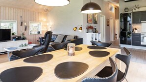 A modern kitchen with a black refrigerator, a dining area with a wooden table and black chairs, and a living area with a black sofa and a TV. - 6 Person Holiday Home in Hojslev-by Traum (Hojslev)