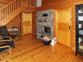 Interior de una cabaña de madera con chimenea de piedra, puertas de madera y una escalera.