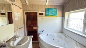 A bathroom with a sink, a bathtub, a window with a view, and wooden walls. - Holiday Home in Otterndorf (Otterndorf)