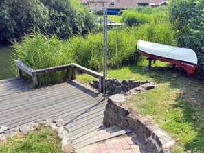 A wooden dock leading to a stone bridge over a water body, with a canoe labeled 'New Zealand 23' on the right.