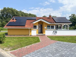A yellow building with a red-tiled roof, a covered porch, and a paved driveway. - Holiday Home in Otterndorf (Otterndorf)