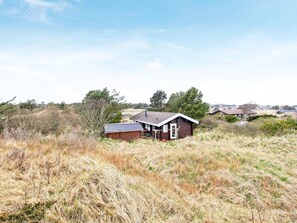A rural cabin with a small porch and a detached garage, surrounded by dry grass and trees. - 6 Person Holiday Home in Bindslev (Bindslev)