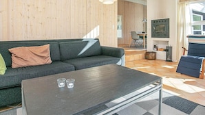 A modern living room with a dark grey sofa, a coffee table with glasses, and a wooden wall. - Tranquil Retreat With Spa - By Traum Ferienwohnungen (Aalbaek)