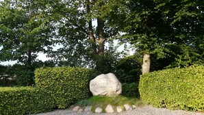 A stone monument with inscriptions, surrounded by neatly trimmed hedges and a gravel path leading to it. - Peaceful Holiday Home in Jutland with Hot Tub (Oksbol)