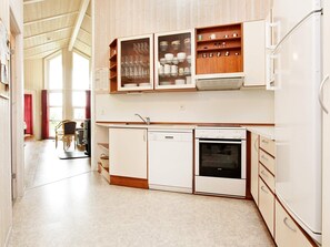 A compact kitchen with white appliances, wooden cabinets, and a view into the dining area. - Holiday Home in Otterndorf (Otterndorf)