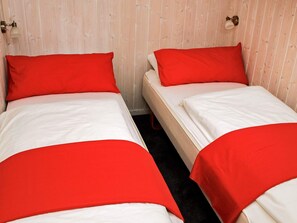 Duas camas de solteiro com roupa de cama vermelha em quarto com paredes de madeira e duas luminárias fixadas na parede.