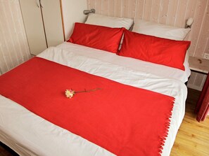 A bed with white and red bedding, a single flower on the bedspread, and a wooden headboard.