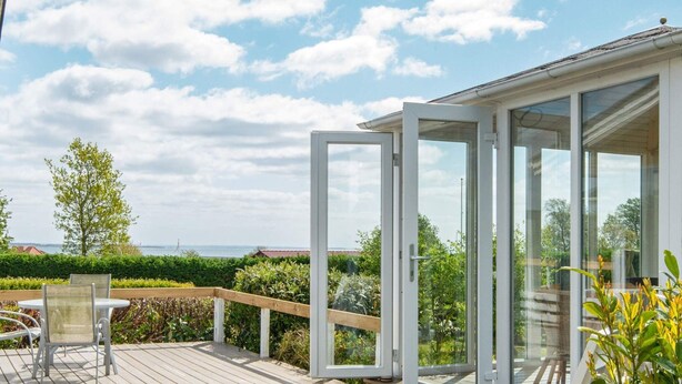 A deck with outdoor seating and a glass door leading to a covered area with a view of the sea. - 6 Person Holiday Home in Hejls (Hejls)