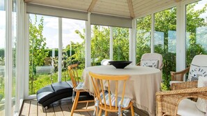 A covered patio with a table and chairs, large windows, and a view of greenery. - 6 Person Holiday Home in Hejls (Hejls)