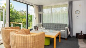 A modern living room with a grey sofa, wicker chairs, a wooden coffee table, and a view of greenery through large windows. - 6 Person Holiday Home in Hejls (Hejls)
