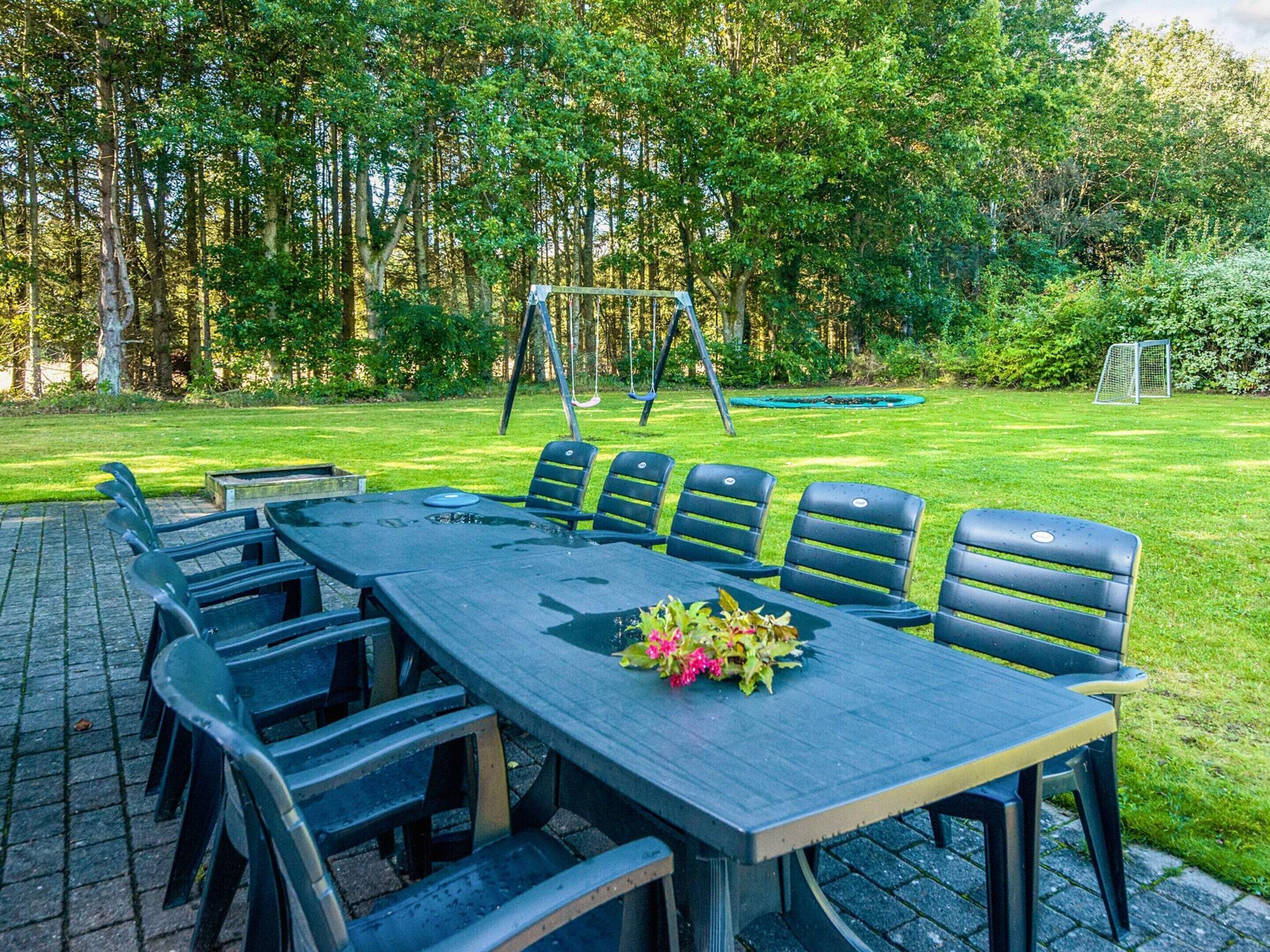 A picnic table with six chairs, a flower arrangement, and a swing set in a grassy outdoor area.