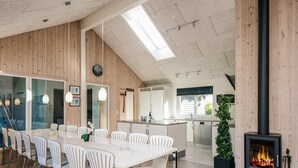A modern kitchen with a central island, a dining area with white chairs, and a fireplace. - Quaint Holiday Home in Fur Jutland near Fjord (Glesborg)