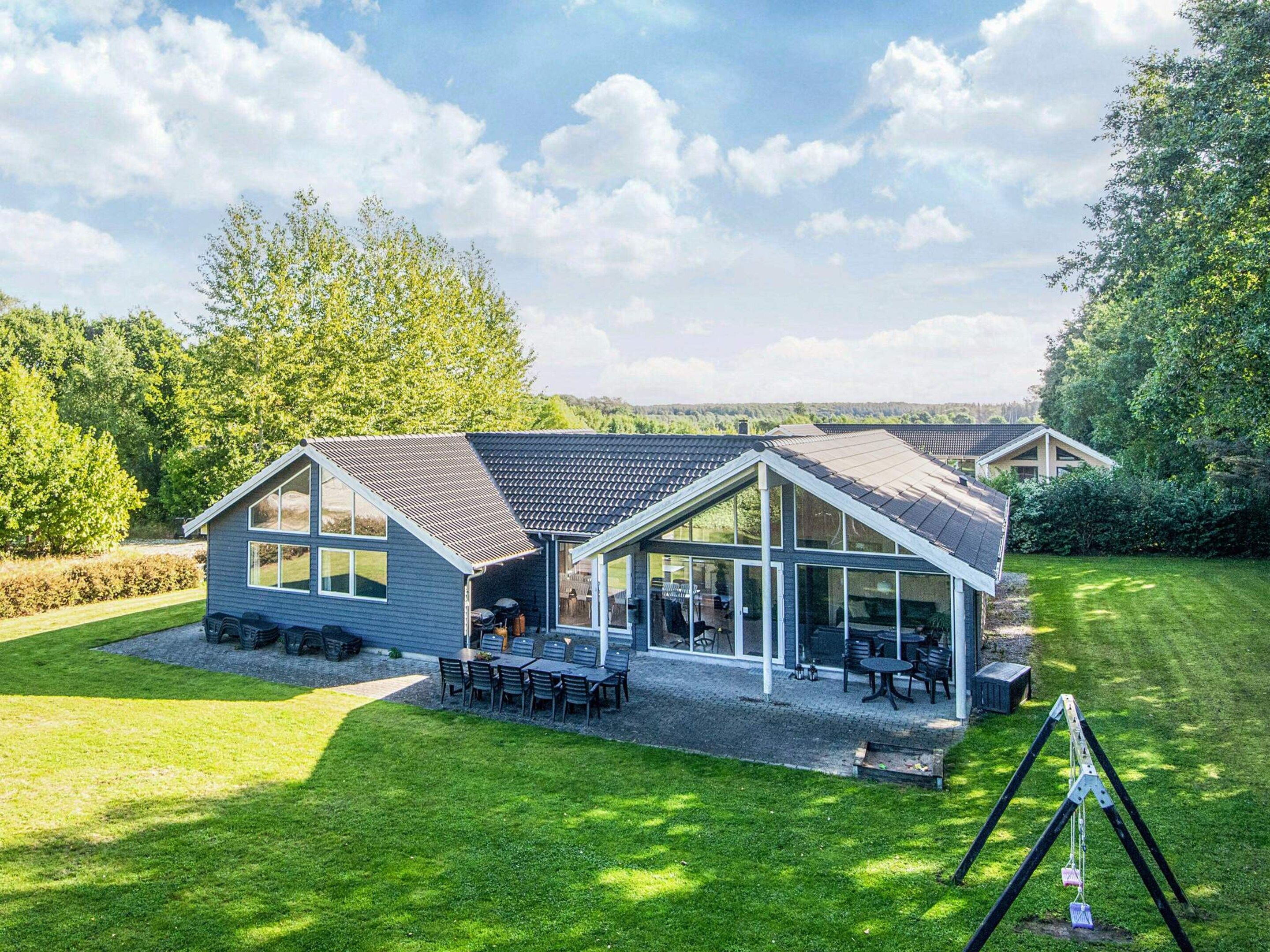 A modern two-story house with a large patio area, a covered outdoor seating space, and a well-maintained lawn.