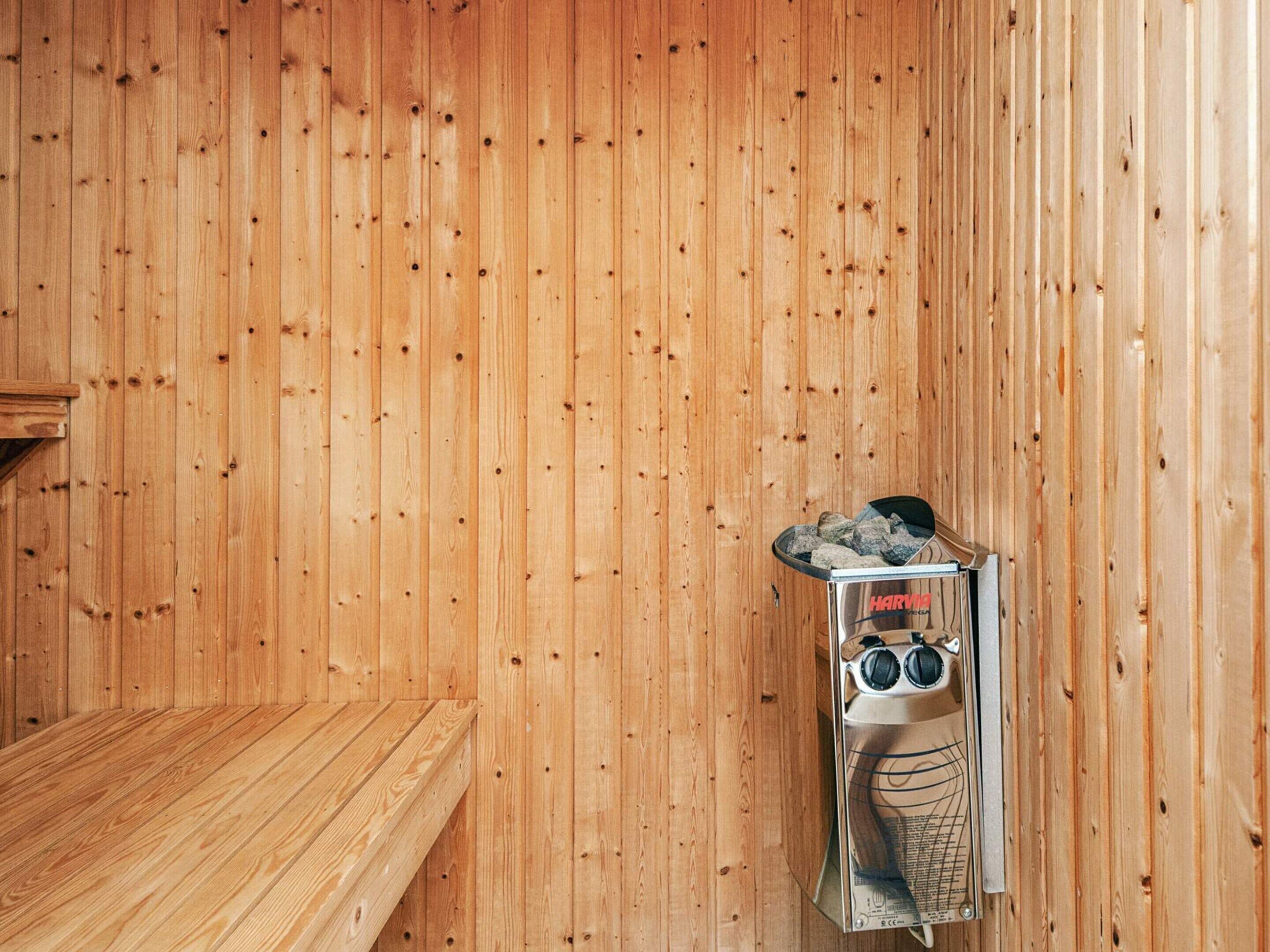 A sauna room with wooden walls, a bench, and a sauna machine labeled "HARVOG."