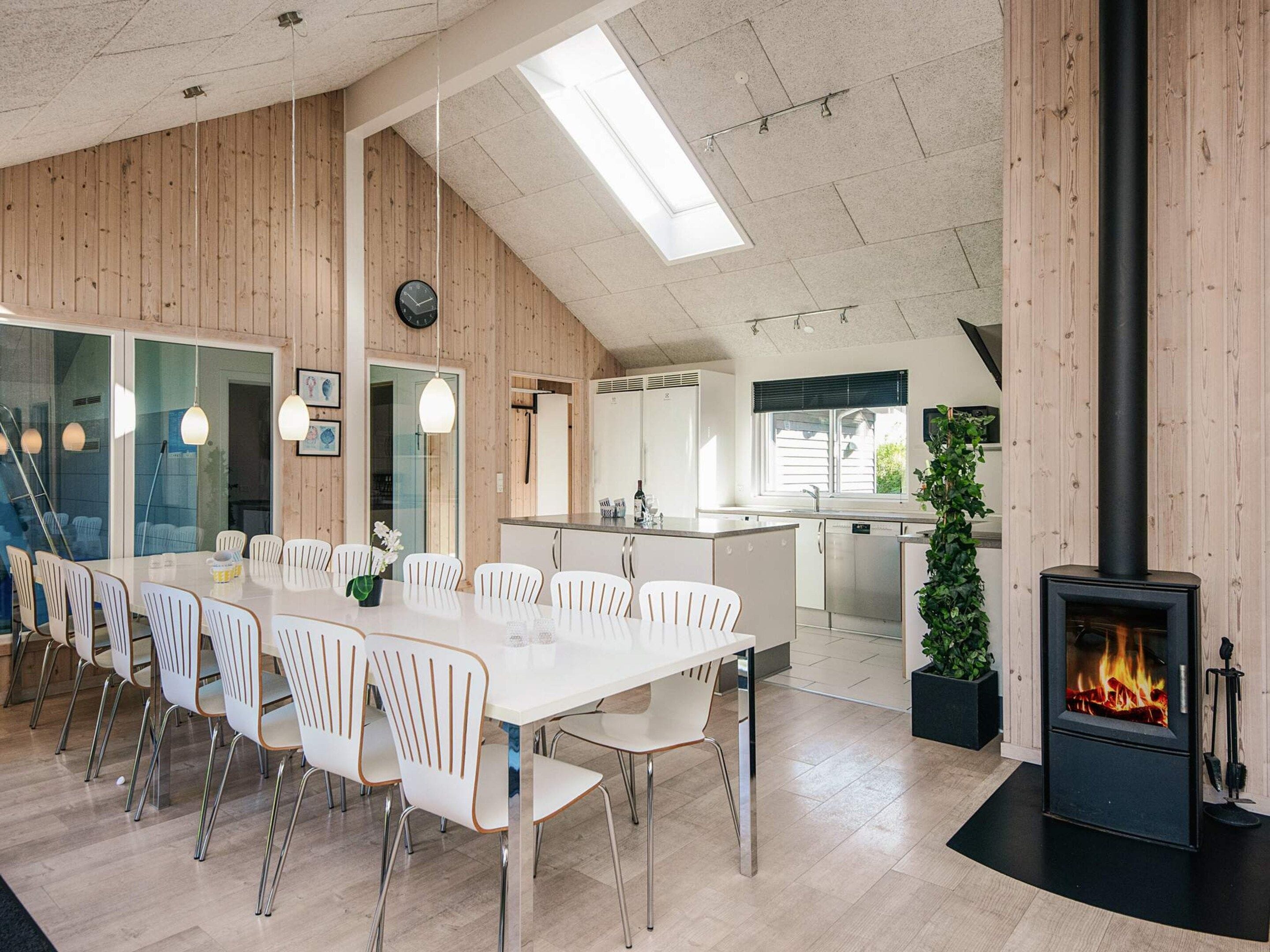 A modern kitchen with a central island, a dining area with white chairs, and a fireplace.