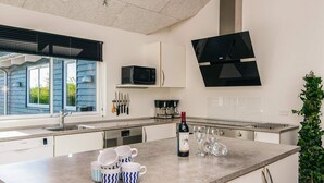 A modern kitchen with white cabinets, a large island, a Bosch dishwasher, a microwave, and a black TV mounted on the wall. - Quaint Holiday Home in Fur Jutland near Fjord (Glesborg)