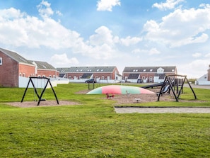 A playground with swings and slides, surrounded by a grassy area and buildings in the background.