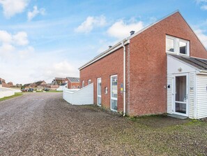 En rød murbygning med en hvid dør og en garageport, en grusvej og en klar himmel.