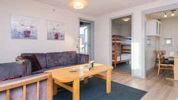 A modern living room with a sofa, a wooden table, and a bunk bed in the background.