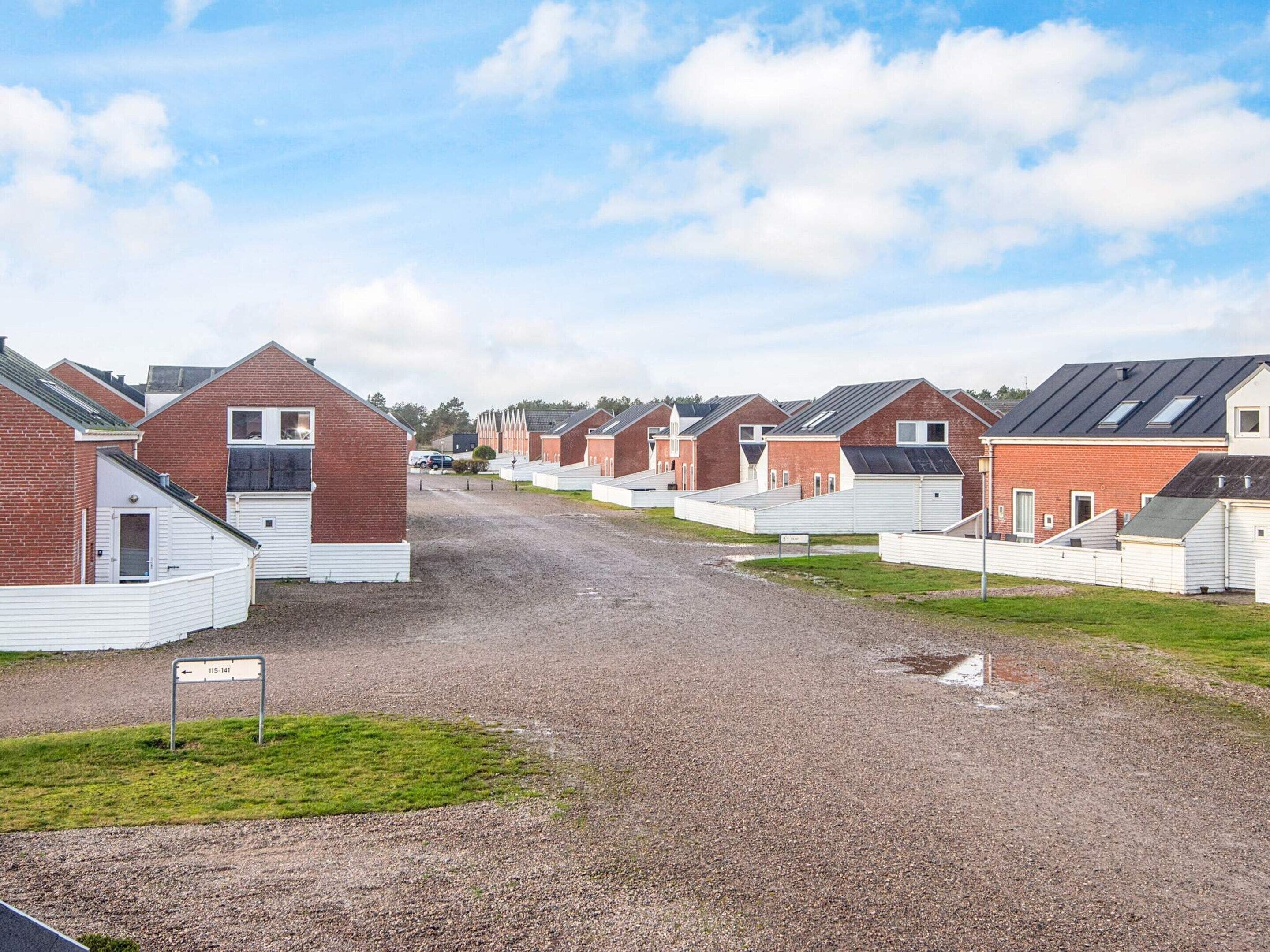 Reihenweise Caravans mit Satteldächern und weißen Fassaden, angeordnet entlang eines Kiesweges, mit einer Grünfläche im Vordergrund.