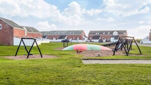Een speeltuin met schommels en glijbanen, omringd door een gazon en bakstenen gebouwen op de achtergrond.