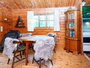 A wooden cabin interior with a dining table, chairs, a cabinet, and a stove. - 4 Person Holiday Home in Farvang (Farvang)
