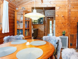 A wooden cabin interior with a dining table, chairs, a cabinet with books, and a hanging light fixture. - 4 Person Holiday Home in Farvang (Farvang)