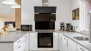 A modern kitchen with white cabinets, a black oven, a microwave, a coffee maker, and pendant lighting. - 5 Star Holiday Home in Nordborg (Nordborg)