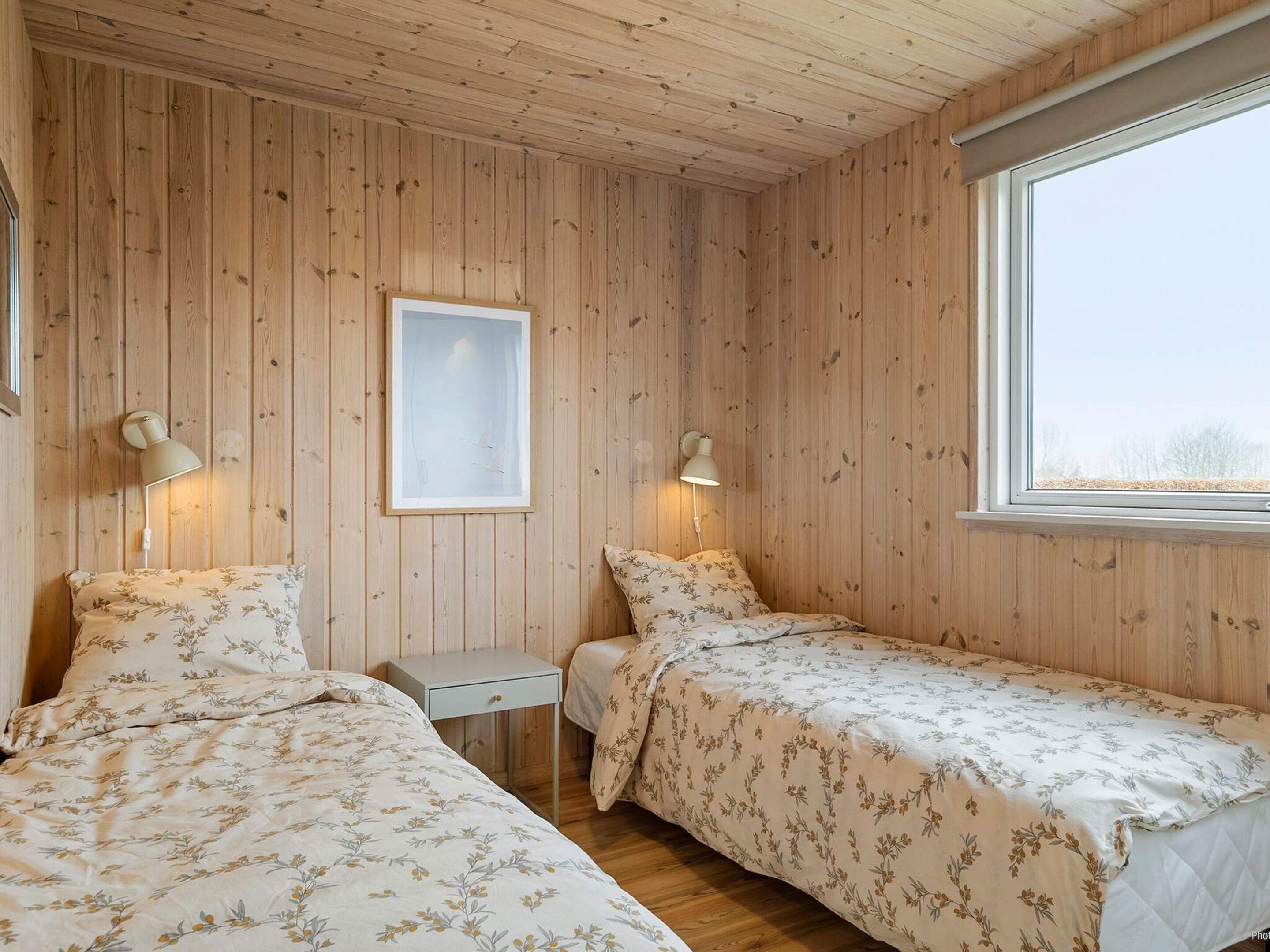 A room with wooden walls, two beds with floral bedding, a small table, and a framed picture.