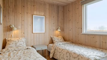 Ett rum med träväggar, två sängar med blommigt sänglinne, ett litet bord och en inramad tavla.