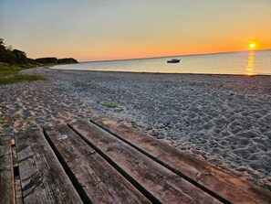 A wooden boardwalk leading to a beach with a boat on the water and a sunset in the background. - 5 Star Holiday Home in Nordborg (Nordborg)