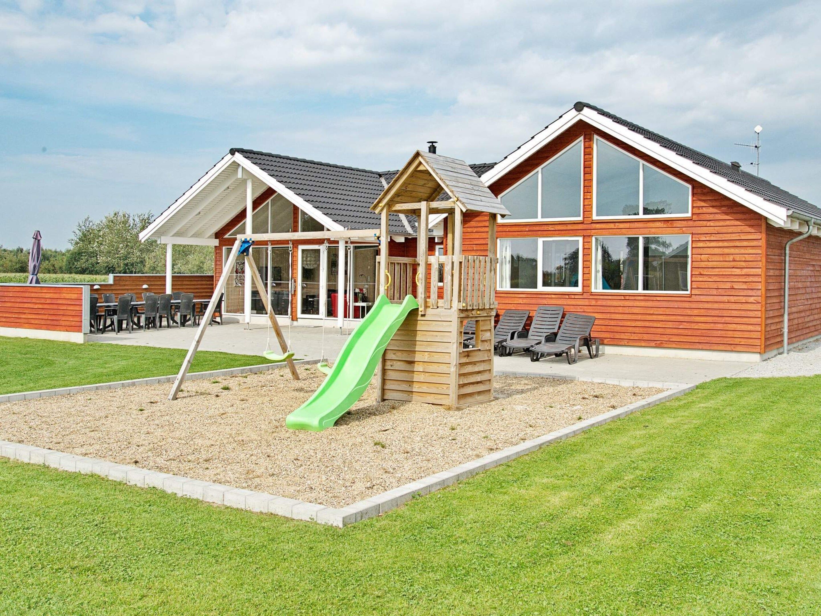 A playground with a slide and swings, adjacent to a building with large windows and a sloped roof.