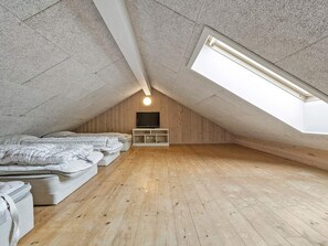 A small, sloped ceiling room with a wooden floor, a bed, a TV on a wooden stand, and a skylight. - 5 Star Holiday Home in Nordborg (Nordborg)