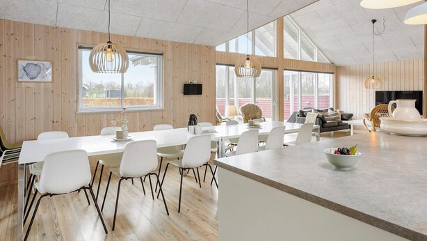 A spacious dining area with a long table, white chairs, and pendant lighting. - 5 Star Holiday Home in Nordborg (Nordborg)
