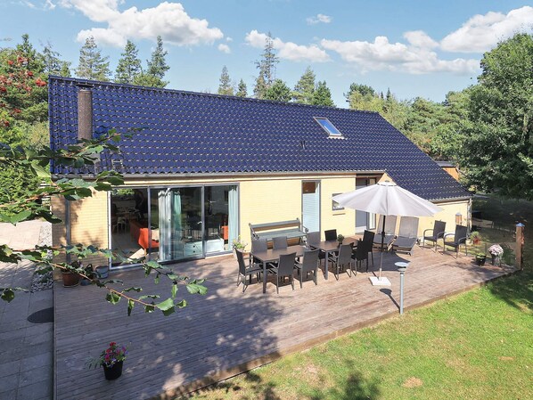A house with a blue tiled roof, a covered patio with outdoor furniture, and a sliding glass door leading to an interior space.