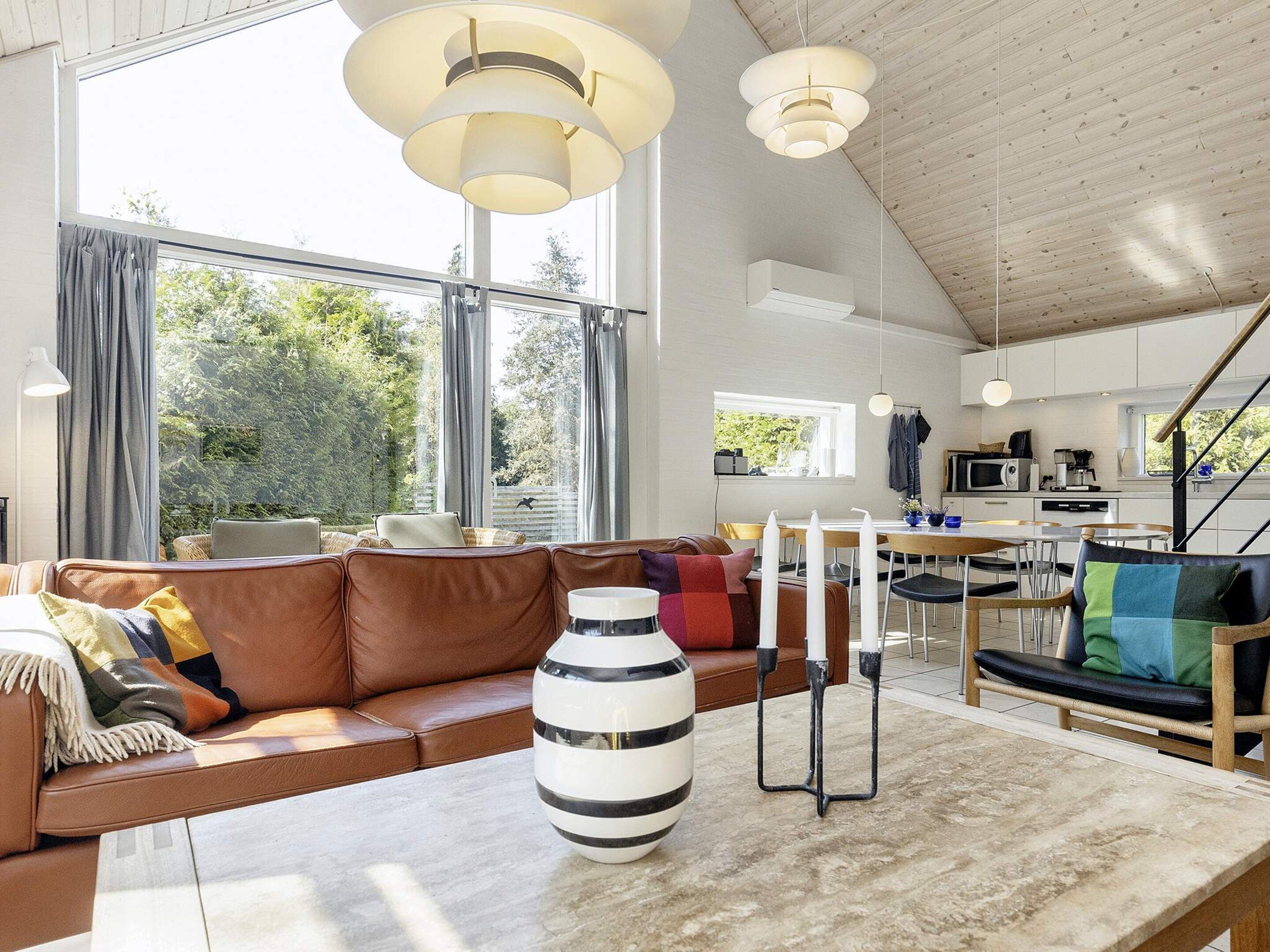 Uma sala de estar moderna com um sofá de couro, uma mesa de jantar e uma cozinha ao fundo.
