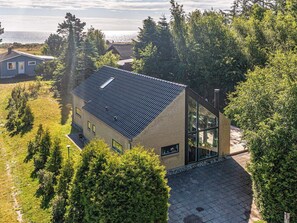 A modern house with a sloped roof, large windows, and a view of the sea.