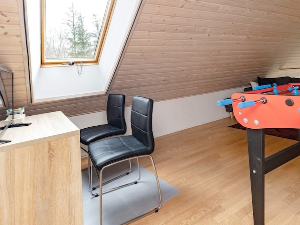 A room with a wooden ceiling, a foosball table, two black chairs, and a desk with a computer monitor.