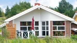 A house with a white exterior, a brick chimney, and a front porch with a red umbrella. - Holiday Home in Otterndorf (Otterndorf)