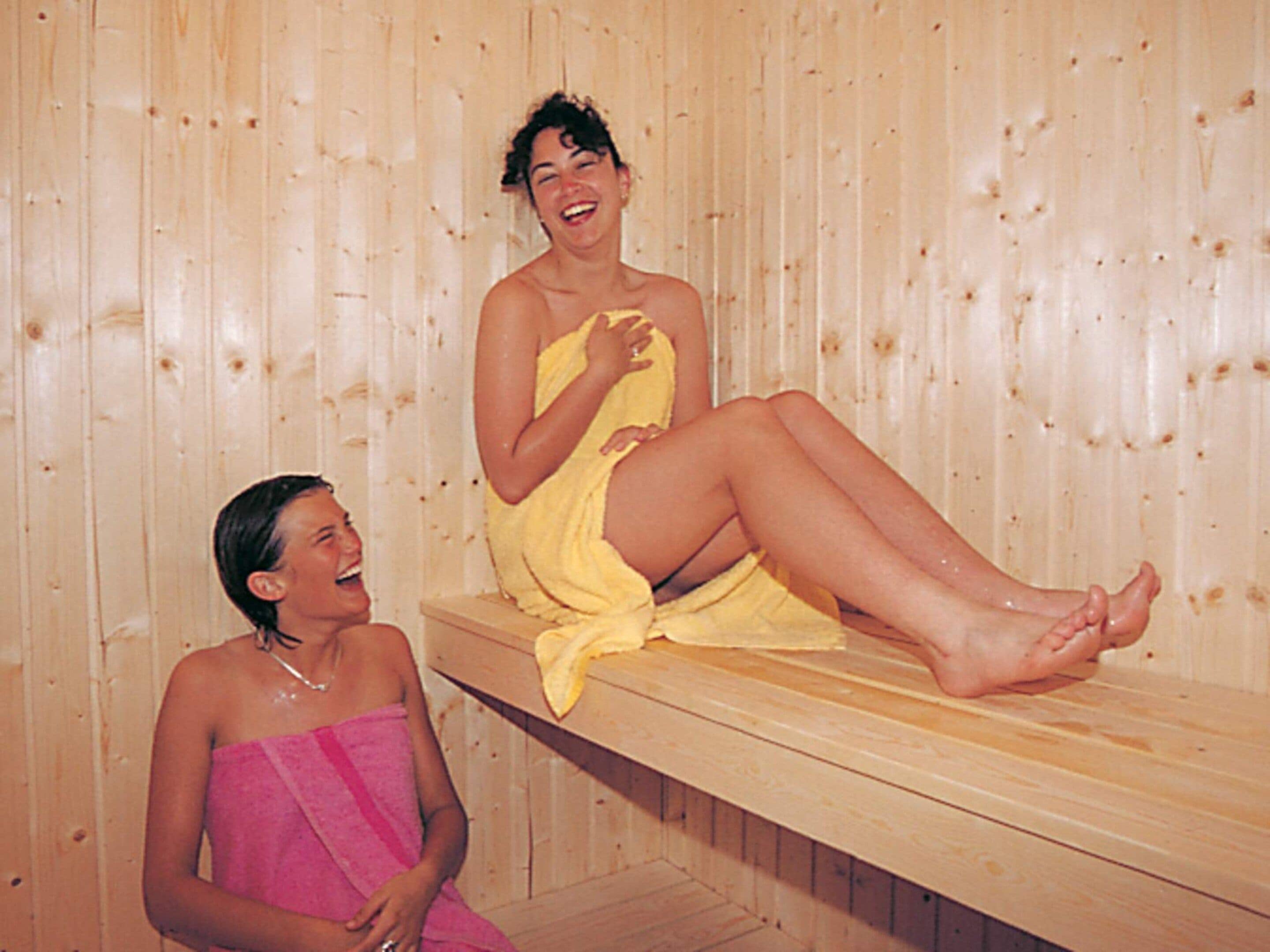 Zwei Personen sitzen in einer Holzsauna mit Bänken.