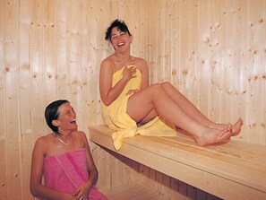 Two individuals seated in a wooden sauna with benches. - Holiday Home in Otterndorf (Otterndorf)
