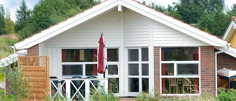 Une maison à l’extérieur blanc, avec une cheminée en briques et un porche à l’avant surmonté d’un parasol rouge.