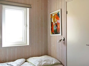 A room with wooden panel walls, a bed with white bedding, a window, and a door. - Holiday Home in Otterndorf (Otterndorf)