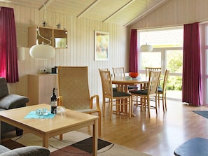 A room with a dining table, chairs, a sofa, a lamp, a painting, and a window with curtains. - Holiday Home in Otterndorf (Otterndorf)