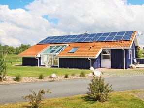 Una casa con techo inclinado, paneles solares, puerta de vidrio y un pequeño porche.