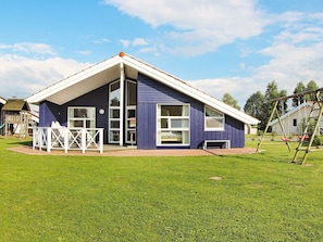 A single-story house with a sloped roof, a fenced patio area, and a swing set. - Holiday Home in Otterndorf (Otterndorf)