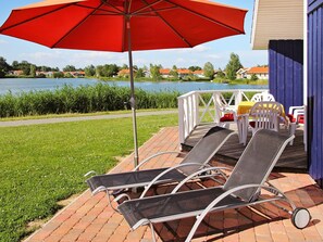 A patio with lounge chairs and an umbrella, overlooking a lake with houses in the background.