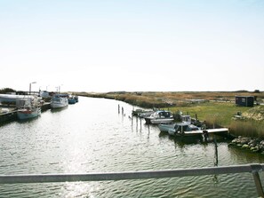 Un canal bordé de bateaux amarrés de chaque côté, une zone herbeuse avec une petite construction et un ciel dégagé.