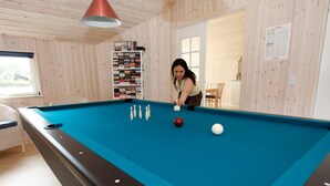 A pool table with balls and a person playing, surrounded by wooden walls and a bookshelf. - Fabulous Holiday Home in Rodby Denmark near Sea (Rodby)