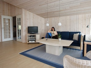 A room with a wooden paneled wall, a television on a stand, a blue sofa, and a wicker chair.